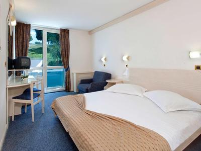 Chambre d'hôtel lumineuse avec lit double, bureau, fauteuil et balcon avec vue sur la montagne.