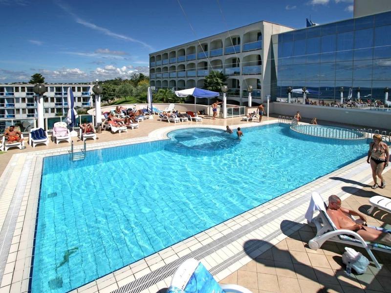 Grand piscine d'hôtel avec chaises longues et invités sous un ciel bleu.
