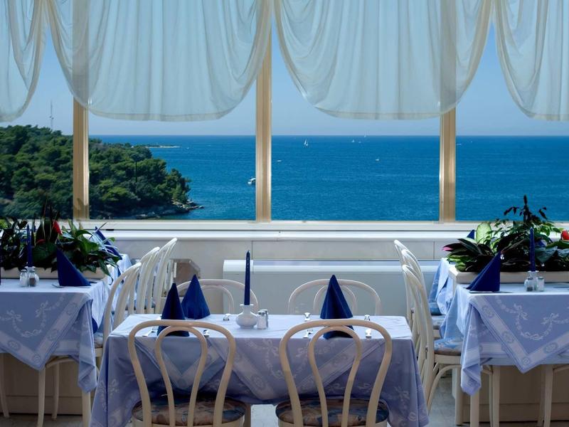 Vue sur la mer avec des tables dressées et des chaises blanches sur une terrasse avec des rideaux.