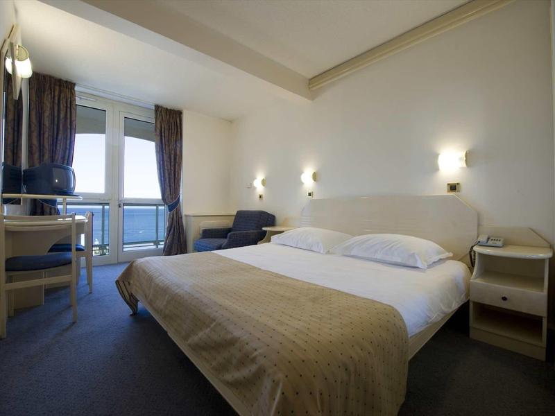 Chambre d'hôtel moderne avec grand lit, coin salon et vue sur balcon.