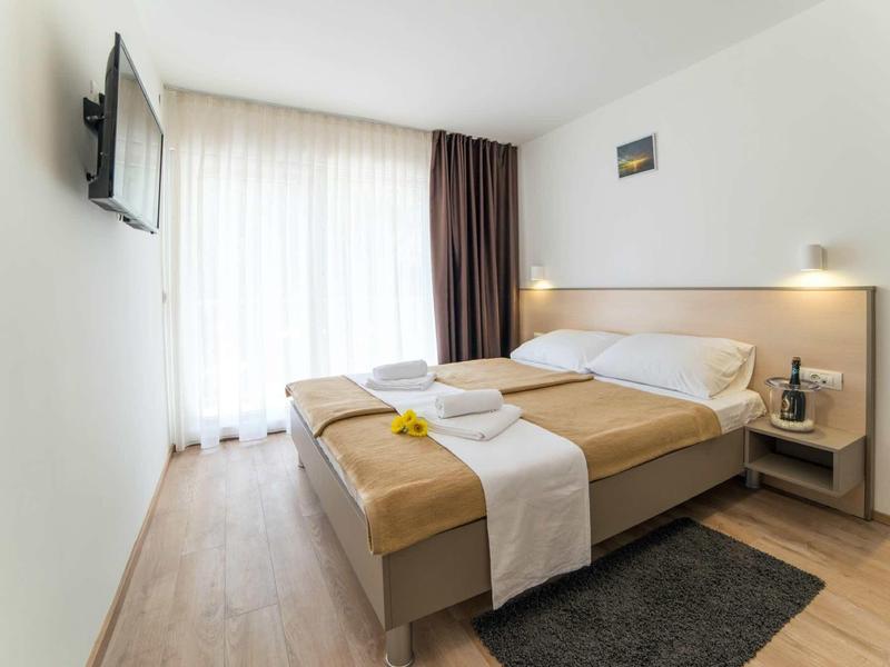 Helles, modernes Schlafzimmer mit Doppelbett, Holzfußboden, großem Fenster und Fernseher an der Wand.