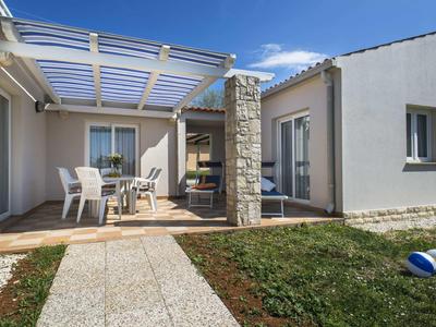 Bungalow moderne avec terrasse, jardin et mobilier extérieur sous un ciel dégagé.