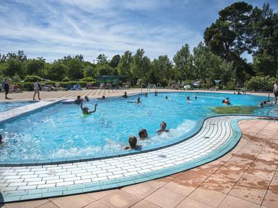 Piscine extérieure animée avec des personnes nageant et se relaxant par une journée ensoleillée.