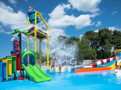 Kolorowy plac zabaw wodny z zjeżdżalniami i funkcjami natryskowymi na zewnątrz w słoneczny dzień.
