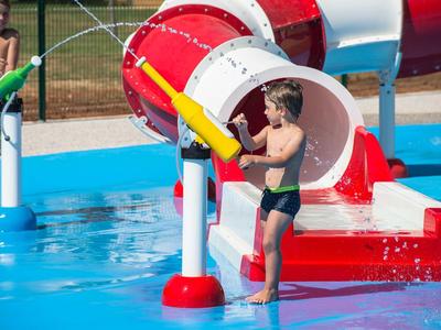 Dzieci bawiące się pistoletami na wodę w zewnętrznym parku wodnym w słoneczny dzień.