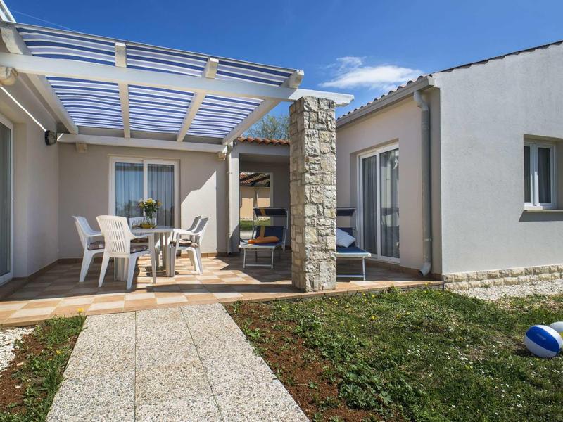 Taras z pergolą, ogrodem i leżakami przy nowoczesnym domu wakacyjnym.