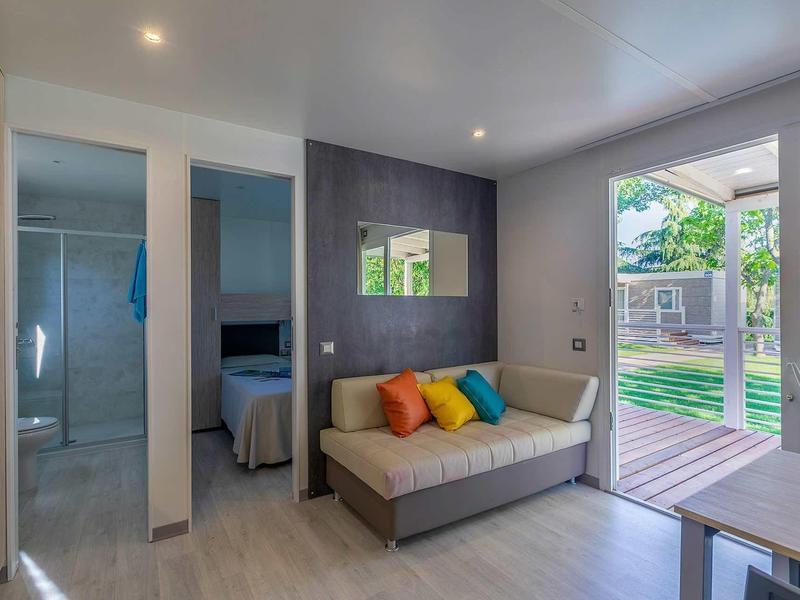 Nowoczesny salon z tarasem, szarą sofą i kolorowymi poduszkami w domku wakacyjnym.