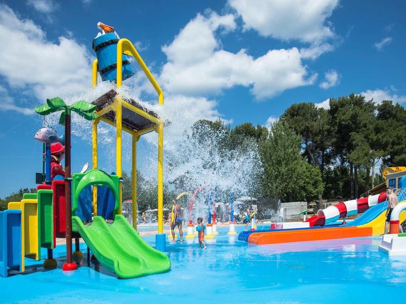 Kolorowy plac zabaw wodny z zjeżdżalniami i funkcjami natryskowymi na zewnątrz w słoneczny dzień.