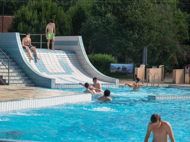 Basen z zjeżdżalnią wodną i ludźmi, otoczony drzewami w tle.