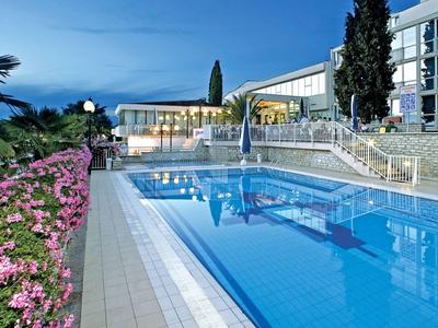 Ein moderner Hotelpool bei Abenddämmerung, umgeben von Blumen und Palmen.