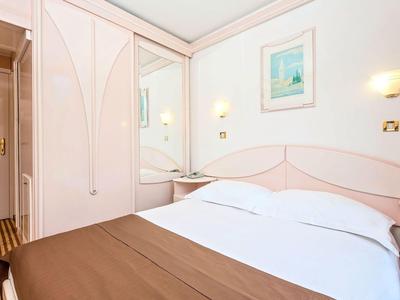 Helles Hotelzimmer mit Doppelbett, brauner Bettdecke, Spiegel und Kleiderschrank.