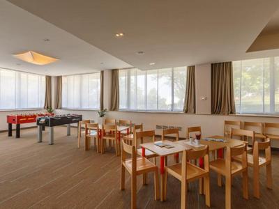Heller Freizeitraum mit Spieltischen und Holzstühlen vor großen Fenstern in einem Hotel.