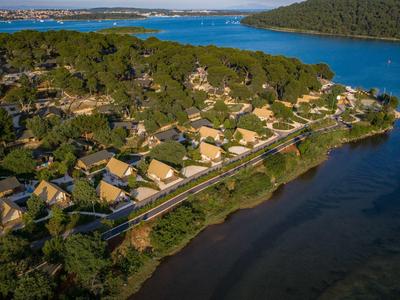 Letecký pohled na resort s bungalovy vedle jezera a zalesněných kopců.