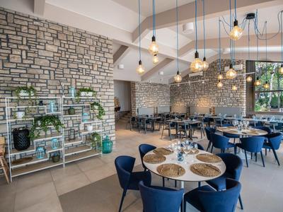 Moderní restaurace s modrými židlemi, kulatými stoly a industriálními nástěnnými lampami.