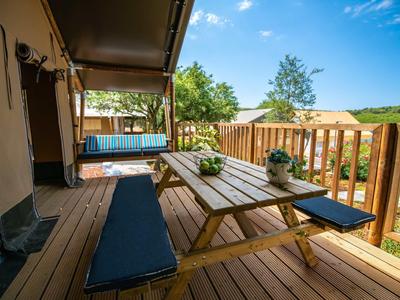 Dřevěná terasa s piknikovým stolem, lavicemi, rostlinami a výhledem na slunečnou krajinu.