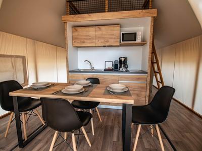 Moderní jídelní kout se stolem a černými židlemi před kuchyňským koutem v bungalovu se stanem.