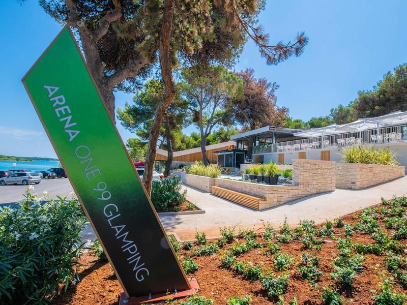 Nowoczesny ośrodek glampingowy z zadbanymi rabatami i widokiem na morze pod bezchmurnym niebem.