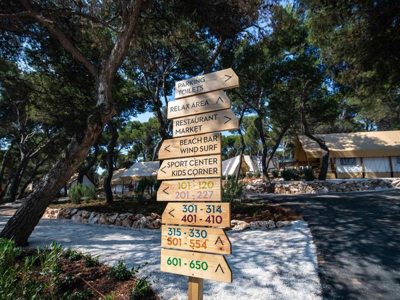 Drogowskaz z wieloma kierunkami w zalesionym parku z domami w tle.