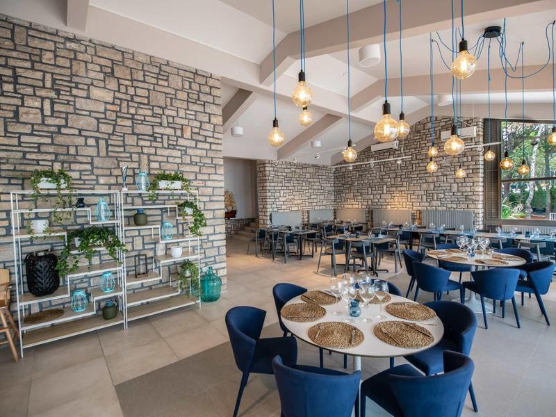 Nowoczesna restauracja z niebieskimi krzesłami, kamienną ścianą i wiszącymi żarówkami w hotelu.