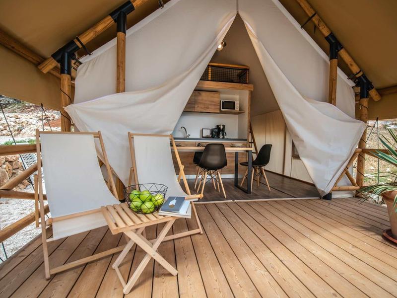 Przytulny taras z drewnianym krzesłem, stolikiem i namiotowym bungalowem w tle.