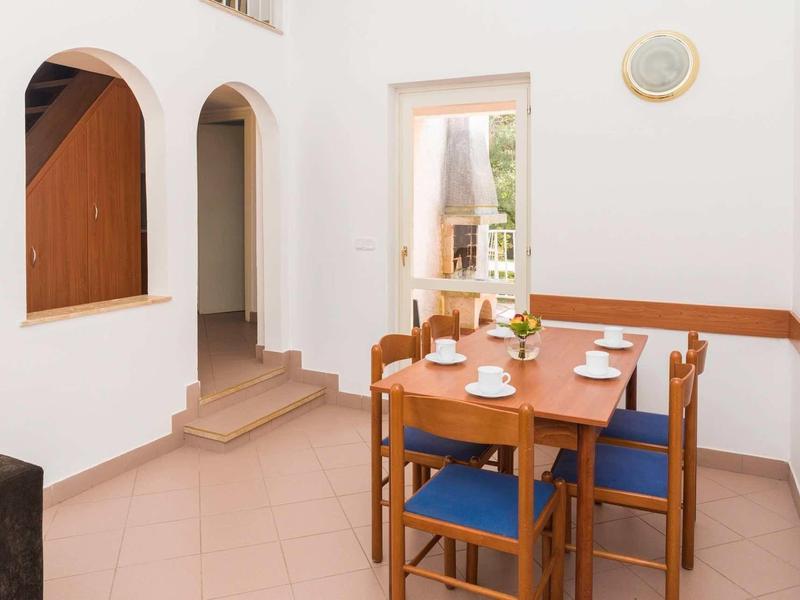 Salle à manger avec table en bois et quatre chaises bleues dans une pièce blanche et lumineuse avec fenêtre en arc.