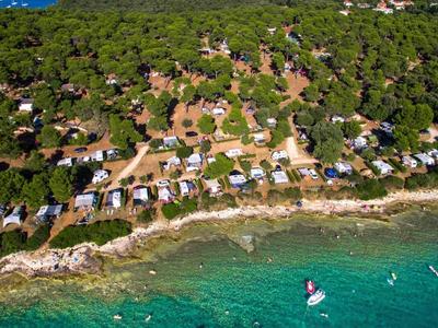 Küste mit grünem Wald, Häusern am Ufer und klarem, türkisfarbenem Wasser mit Booten.