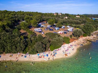 Strand mit weißem Sand, grünem Wasser, Bäumen und Menschen, die am Ufer und auf dem Parkplatz sind.