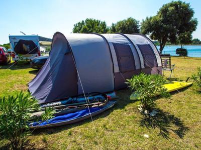 Grande tente grise sur herbe verte avec deux planches de surf et arbres en arrière-plan.