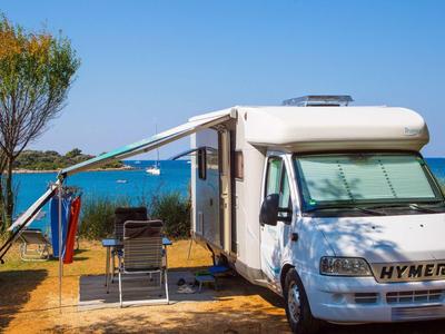 Camping-car avec auvent sur une plage ensoleillée avec chaises et table à l'ombre