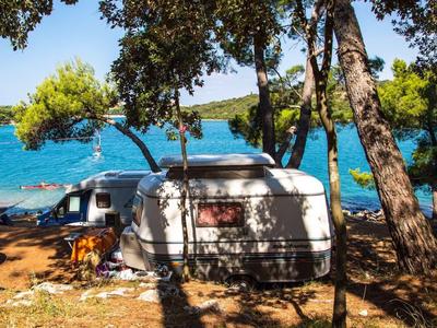 Caravane stationnée parmi des arbres au bord d'un lac avec des bateaux sous un temps ensoleillé