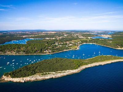 Luftaufnahme einer grünen Insel mit Segelbooten im blauen Meer unter klarem Himmel.