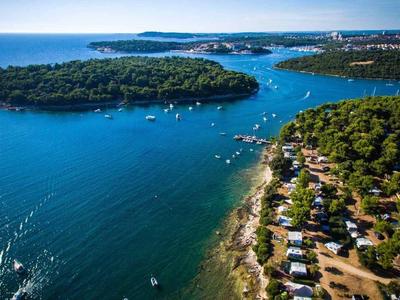 Küstenlandschaft mit blauem Meer, bewaldeter Insel und Campingplatz am Ufer.