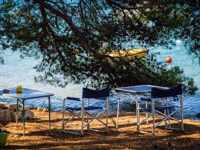 Quatre chaises avec une petite table sur la plage sous des arbres ombragés donnant sur la mer.