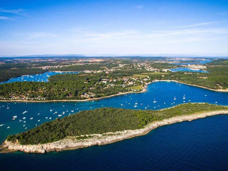 Luftaufnahme einer grünen Insel mit Segelbooten im blauen Meer unter klarem Himmel.