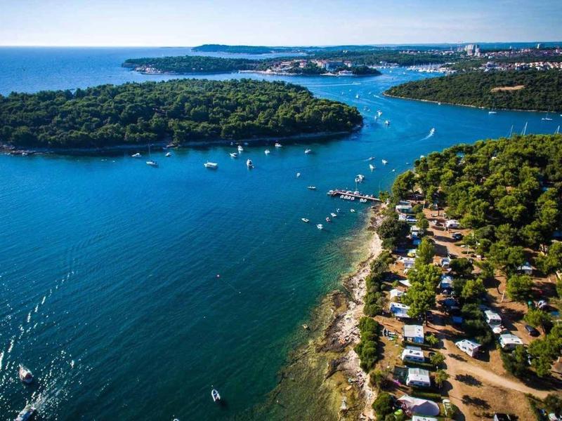 Küstenlandschaft mit blauem Meer, bewaldeter Insel und Campingplatz am Ufer.
