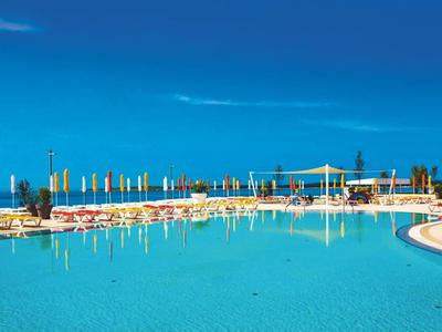 Großer Hotelpool mit Liegestühlen und Sonnenschirmen unter klarem blauem Himmel