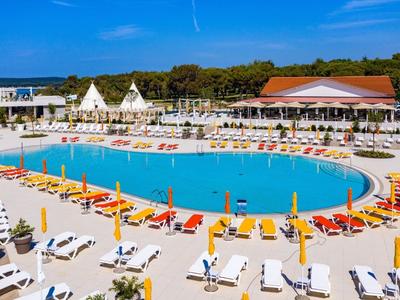 Groot hotelzwembad met ligbedden en parasols onder een blauwe lucht