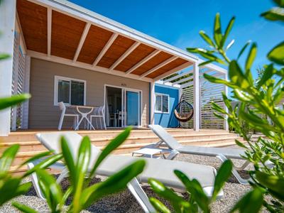 Nowoczesne patio z drewnianym tarasem, leżakiem, zestawem stołowym i przesuwnymi drzwiami pod błękitnym niebem.