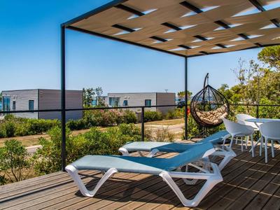 Nowoczesny taras z leżakami, wiszącym fotelem i widokiem na ocean pod pergolą.