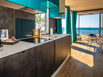 Jasny pokój hotelowy z aneksem kuchennym i balkonem z widokiem na morze.