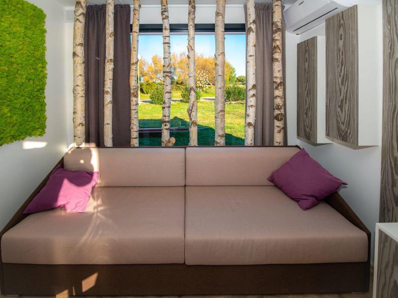 Przytulna beżowa sofa z fioletowymi poduszkami w nowoczesnym pokoju z dekoracją natury.