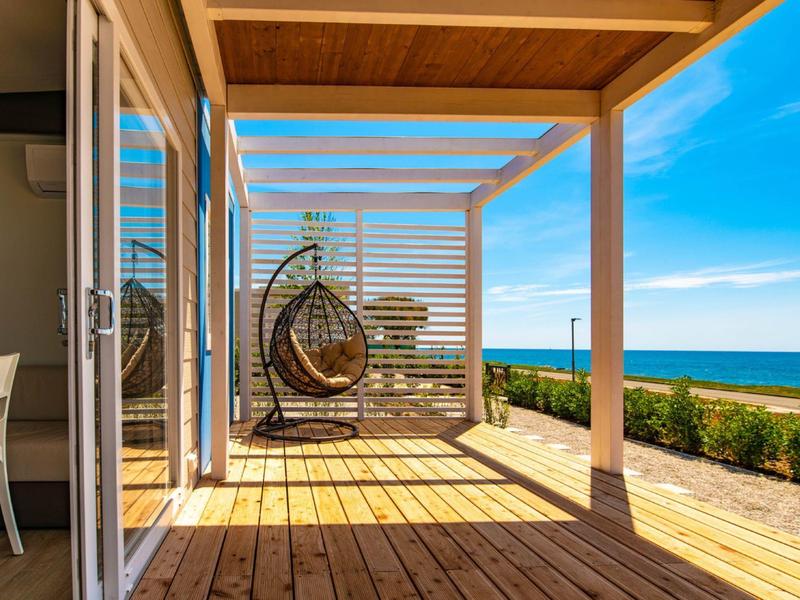 Drewniany taras z wiszącym fotelem z widokiem na ogród i morze pod niebieskim niebem.