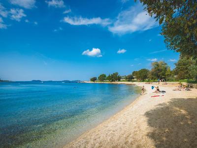 Strand mit klarem blauem Wasser, Sand und vereinzelt liegenden Menschen unter blauem Himmel.