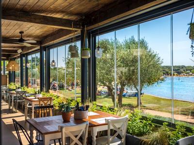 Terrasse eines Restaurants mit Tischen und Stühlen mit Blick auf See und Bäume.