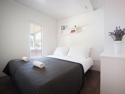 Modernes Hotelzimmer mit Doppelbett, weißen Wänden, dunkler Bettdecke und minimaler Dekoration.