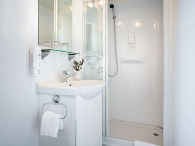 Kompaktes Badezimmer mit weißem Waschbecken, Dusche und modernem Design in einem Hotelzimmer.