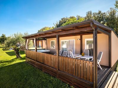 Gemütliche Ferienhütte mit Holzveranda und Liegestühlen, umgeben von Rasen und Bäumen.