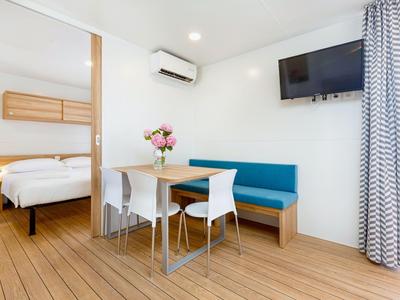 Moderner Hotelraum mit Esstisch, Sesseln, Sofa, Schlafzimmer und TV an der Wand.