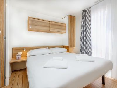 Helles Schlafzimmer mit Doppelbett, Holzvertäfelung und großen Fenstern mit Vorhängen.