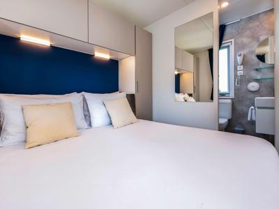 Kompaktes Hotelzimmer mit Doppelbett, Beleuchtung, und offenem Bad mit Dusche.